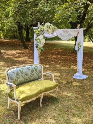Arche de cérémonie champêtre décorée d'hortensias, renoncules et feuillage vert, avec canapé vintage.