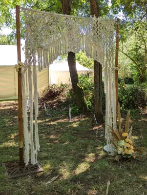 Arche de ceremonie boheme avec macrame, pampas et roses peche pour un mariage en pleine nature.