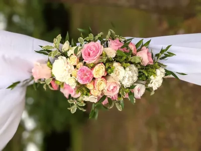 Détail de composition florale d'arche de mariage, roses roses, crèmes, jaunes et carnations blanches sur drapé blanc.