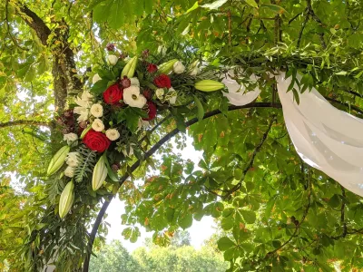 Gros plan sur la composition florale d'une arche de mariage, avec roses rouges, lys blancs et feuillage vert varié.