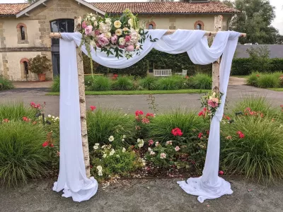 Arche de mariage classique en bouleau et tissu blanc, décorée de compositions florales roses et blanches pour la cérémonie.