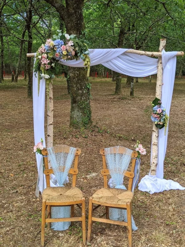 Garden-style floral arch for a wedding ceremony, featuring blue hydrangeas, pastel roses, roses, and foliage, at Domaine de la Forge.