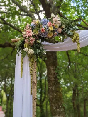 Détail d'une arche florale champêtre et bohème, avec hortensias bleus, roses pâles et feuillage généreux pour un mariage.