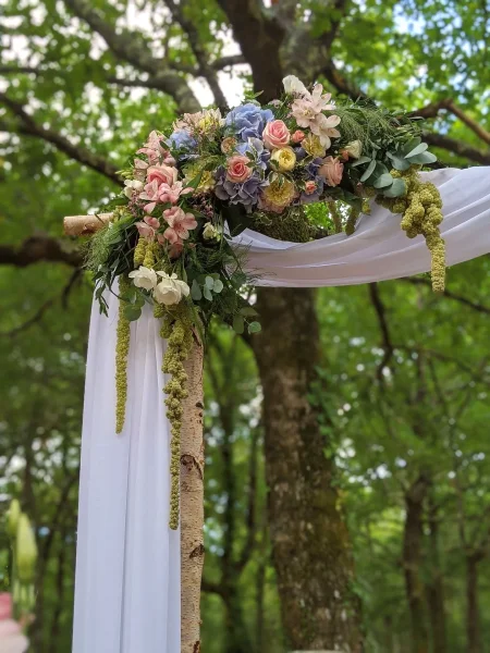 Détail d'une arche florale champêtre et bohème, avec hortensias bleus, roses pâles et feuillage généreux pour un mariage.