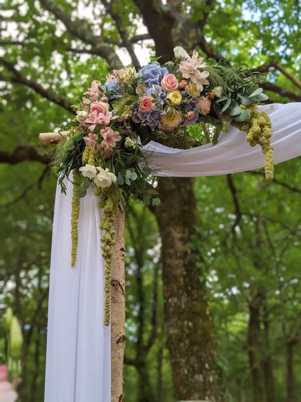Detail of a countryside-inspired and bohemian floral arch, featuring blue hydrangeas, delicate blush roses, and abundant foliage for a wedding.
