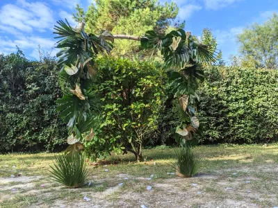 Arche florale de mariage exotique avec grandes feuilles de monstera, palmes dorées et anthuriums blancs, pour une cérémonie en plein air.