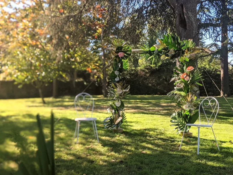 Exotic-style ceremony floral arch with Monstera leaves, palms, and pink anthuriums for a wedding