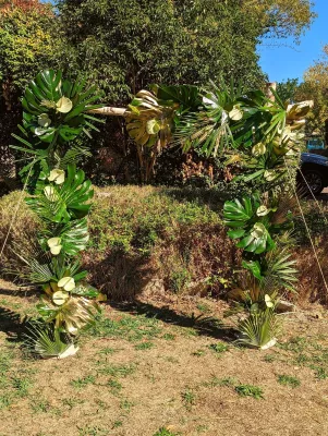 Arche florale de mariage style exotique avec feuilles de monstera, palmiers verts et dorés, fleurs blanches.