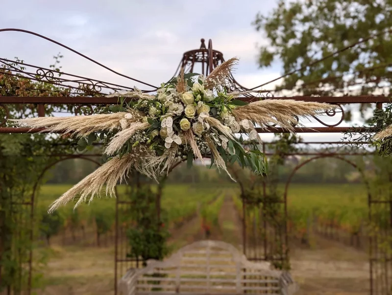 Bohemian floral arch decoration with voluminous pampas grass, cream roses and green foliage for an outdoor wedding.