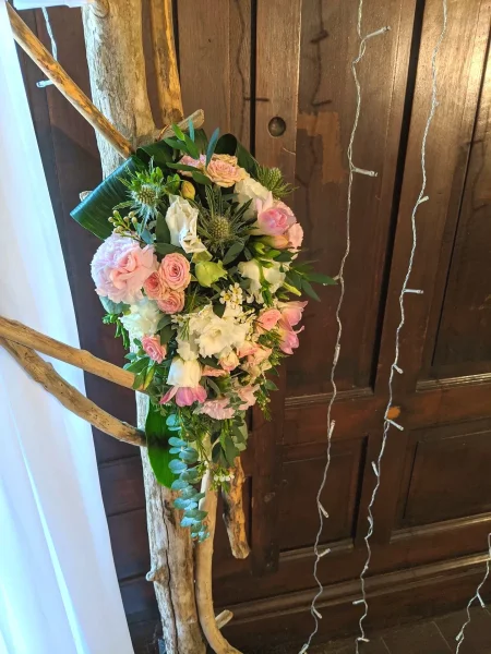 Gros plan sur une composition d'arche florale avec roses, lisianthus, chardons et feuillage vert sur branches de bois.