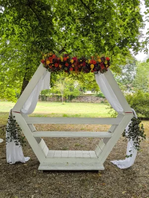 Arche florale hexagonale avec roses orange, fuchsia, chrysanthèmes jaunes et feuillage vert.