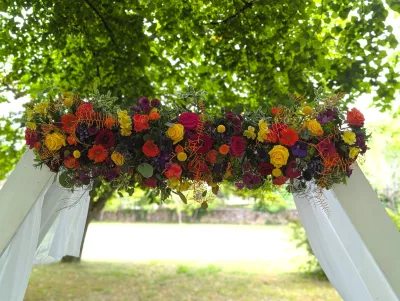 Détail de l'arche florale avec roses orange, fuchsia, chrysanthèmes jaunes et feuillage.