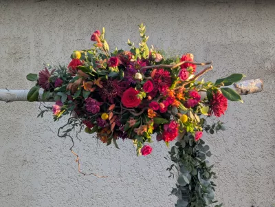Arche florale bohème champêtre pour mariage, avec roses rouges, dahlias bordeaux et feuillage eucalyptus vert.