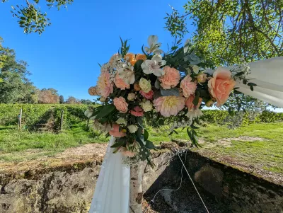 Détail d'une arche florale champêtre avec roses pêche, dahlias corail et feuillage luxuriant pour une cérémonie de mariage.