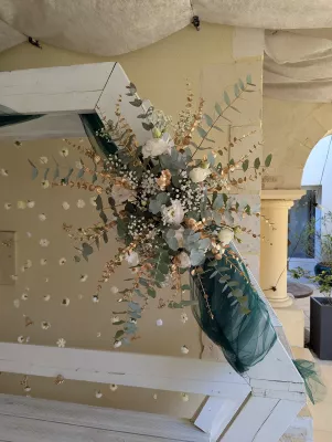 Arche florale de mariage bohème élégante avec roses blanches, eucalyptus vert et doré, et tulle émeraude.