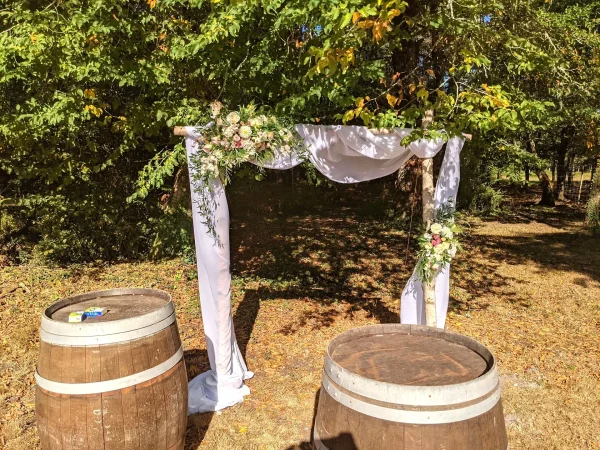 Arche de cérémonie champêtre décorée de draperies blanches, de roses et de feuillage vert pour un mariage au Domaine du Vautrait.