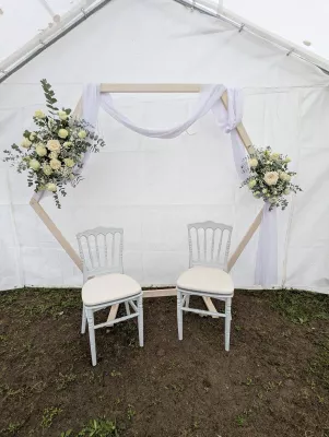 Arche florale de mariage hexagonale décorée de bouquets de roses crème, gypsophile et eucalyptus pour une cérémonie élégante.