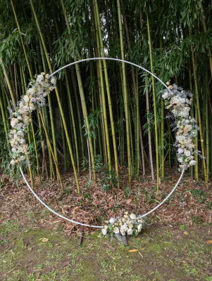 Arche de mariage circulaire moderne décorée de roses poudrées, eustoma et feuillage argenté devant une bambouseraie.