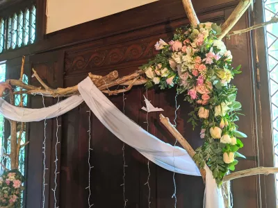 Arche florale décorative avec roses, lisianthus, alstroemeria et feuillage, agrémentée de voilage et lumières.