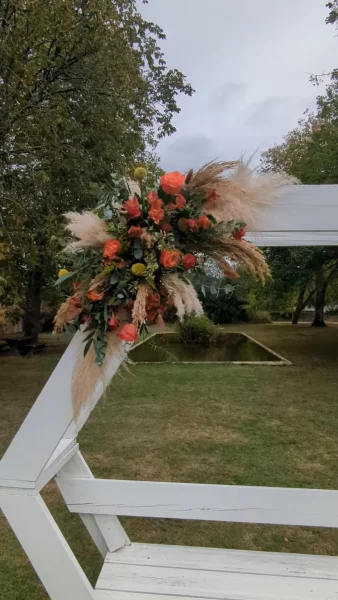 Sophisticated rustic floral arch with orange roses, pampas grass, and eucalyptus for an outdoor wedding.