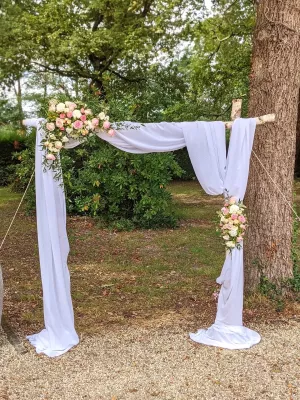 Arche florale de mariage classique avec drapé blanc et compositions de roses roses, crèmes, jaunes et feuillage vert.