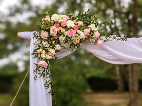 Composition florale latérale d'arche de mariage, roses roses, crèmes, jaunes et feuillage tombant, style classique.