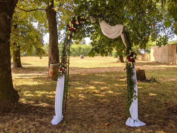 Arche florale de mariage classique ornée de roses rouges et lys blancs, entourée de feuillage vert pour une cérémonie extérieure à Saint-Aubin-de-Médoc.