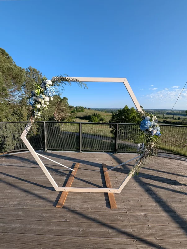 Arche de mariage hexagonale décorée de fleurs bleues et blanches, hortensias, roses et eucalyptus, style moderne champêtre.