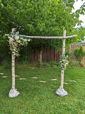 Grande arche de mariage champêtre en bois de bouleau, décorée de compositions florales de roses, hortensias et eucalyptus.