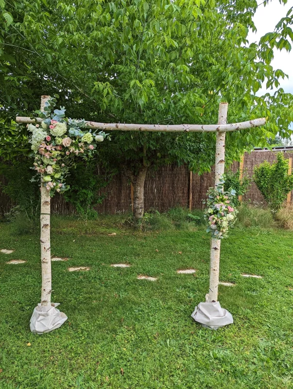 Grande arche de mariage champêtre en bois de bouleau, décorée de compositions florales de roses, hortensias et eucalyptus.