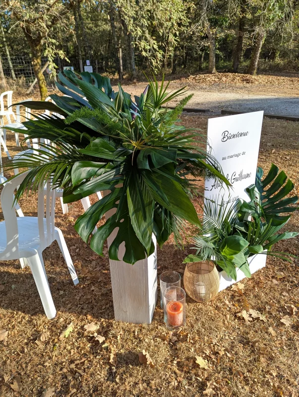 Wedding welcome sign surrounded by grand arrangements of tropical foliage on white columns.
