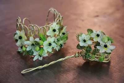 Bijoux floraux champêtres incluant un bracelet et un pic à cheveux avec petites fleurs blanches, feuillage panaché et fil doré.