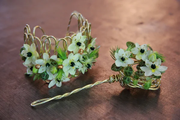 Bijoux floraux champêtres incluant un bracelet et un pic à cheveux avec petites fleurs blanches, feuillage panaché et fil doré.
