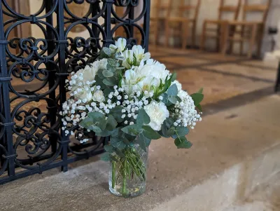 Bouquet de cérémonie avec roses blanches, alstroemerias, gypsophile et eucalyptus dans un vase en verre.