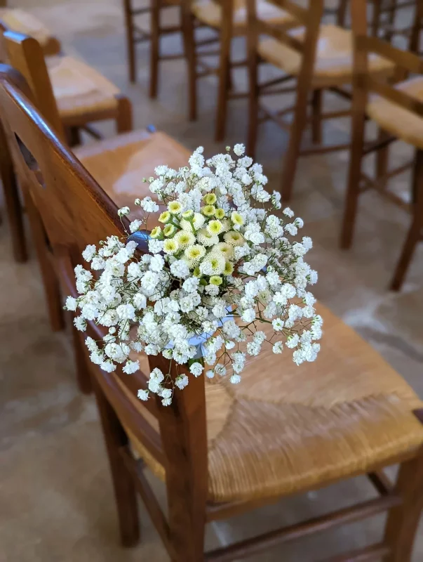 Close-up of a ceremony chair decor featuring white gypsophila and delicate yellow blooms, in a charming country garden style.