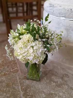 Bouquet de table de cérémonie avec hortensias blancs, gypsophila et feuillage vert, dans un style doux et lumineux.