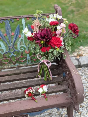 Bouquet de lancer et boutonnières classiques pour un mariage d'été, avec dahlias bordeaux, roses et feuillage vert.