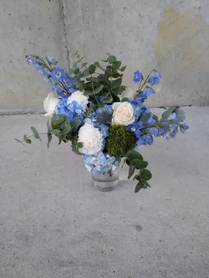Petit bouquet à lancer champêtre avec hortensias bleus, roses blanches et chardons, parfait pour un mariage de printemps.