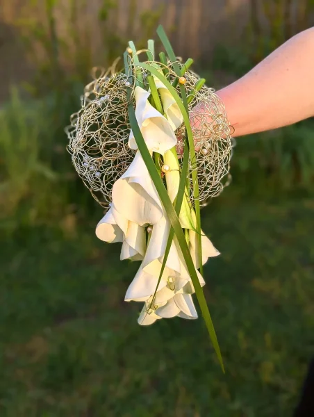 Bouquet de mariée moderne en cascade d'arums blancs, structuré par un maillage doré et des perles pour un mariage élégant.