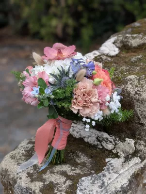 Romantic organic bridal bouquet with pink carnations, peach roses, blue thistles, and orchids.
