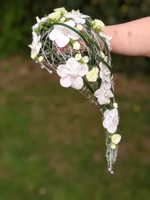 Bouquet de mariée moderne et classique en cascade, composé d'orchidées blanches et de petites roses crème, avec une structure filaire.