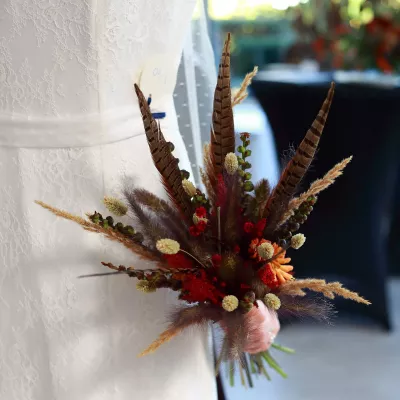 Bouquet de mariée bohème texturé avec plumes naturelles, graminées séchées et petites fleurs rouges pour un salon.