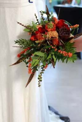 Bouquet de mariée bohème avec renoncules, œillets, gousses de lotus séchées et plumes.