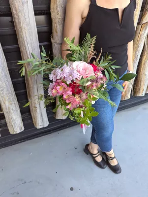 Romantic organic bridal bouquet featuring pink roses, red alstroemerias, and green foliage for a wedding.