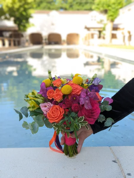 Bouquet de mariée aux couleurs vives: roses orange, fuchsia, chrysanthèmes jaunes et feuillage vert.