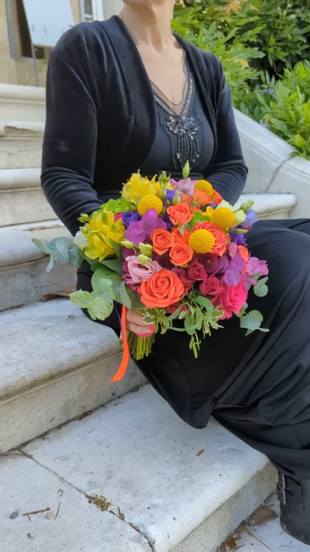 Bouquet de mariée champêtre sophistiqué avec roses orange, chrysanthèmes jaunes et fleurs violettes.