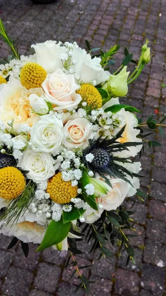 Bouquet de mariée champêtre, composé de roses pâles, craspedia jaune et chardons bleus, pour un mariage printanier.