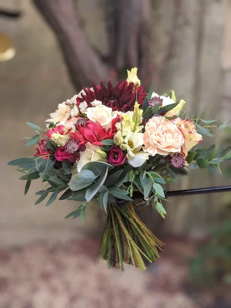 Bouquet de mariee champetre avec roses creme, dahlias bordeaux, oeillets peche et feuillage eucalyptus, mariage d'ete.