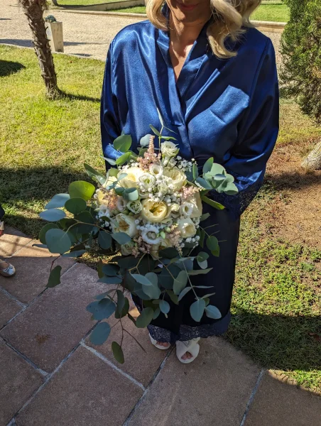 Bouquet de mariée champêtre, avec roses crèmes, eucalyptus, gypsophile et astilbe, tenu par la mariée.