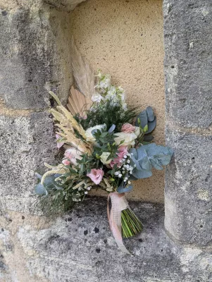 Sophisticated rustic bridal bouquet with roses, eucalyptus and pampas grass, resting on a stone wall.